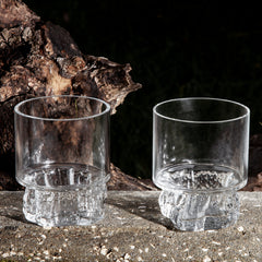 Two glasses in front and a tree trunk in background. 