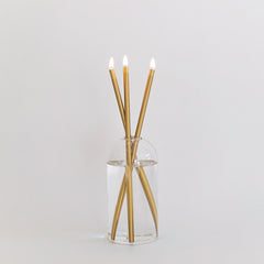 Everlasting candle made from 3 gold colored metal rods in a glass container on a white background