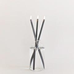 Everlasting candle made from 3 black metal rods in a glass container on a white background