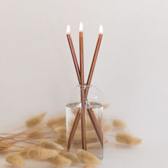 Everlasting candle made of 3 copper colored metal rods in a glass container on a white background and pampas