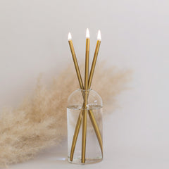 Everlasting candle made of 3 gold colored metal rods in a glass container on a white background and pampas