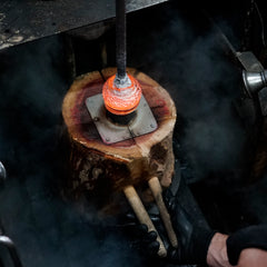 Glob of molten glass into a wooden carved mold.